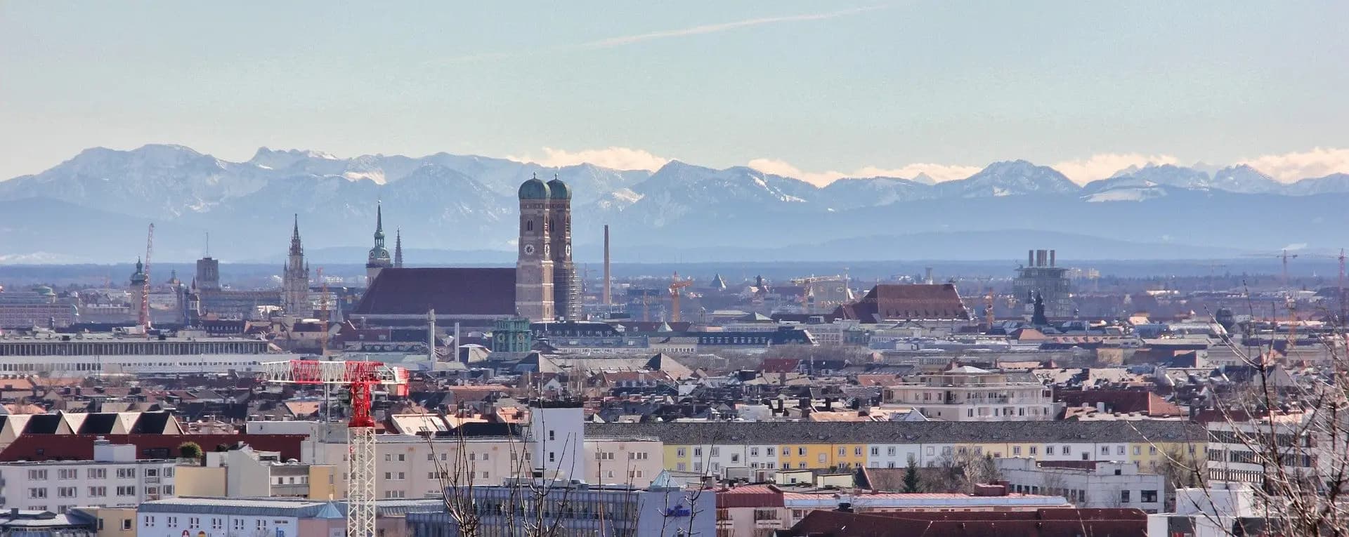 Panorama von München mit Frauenkirche und Alpen im Hintergrund.